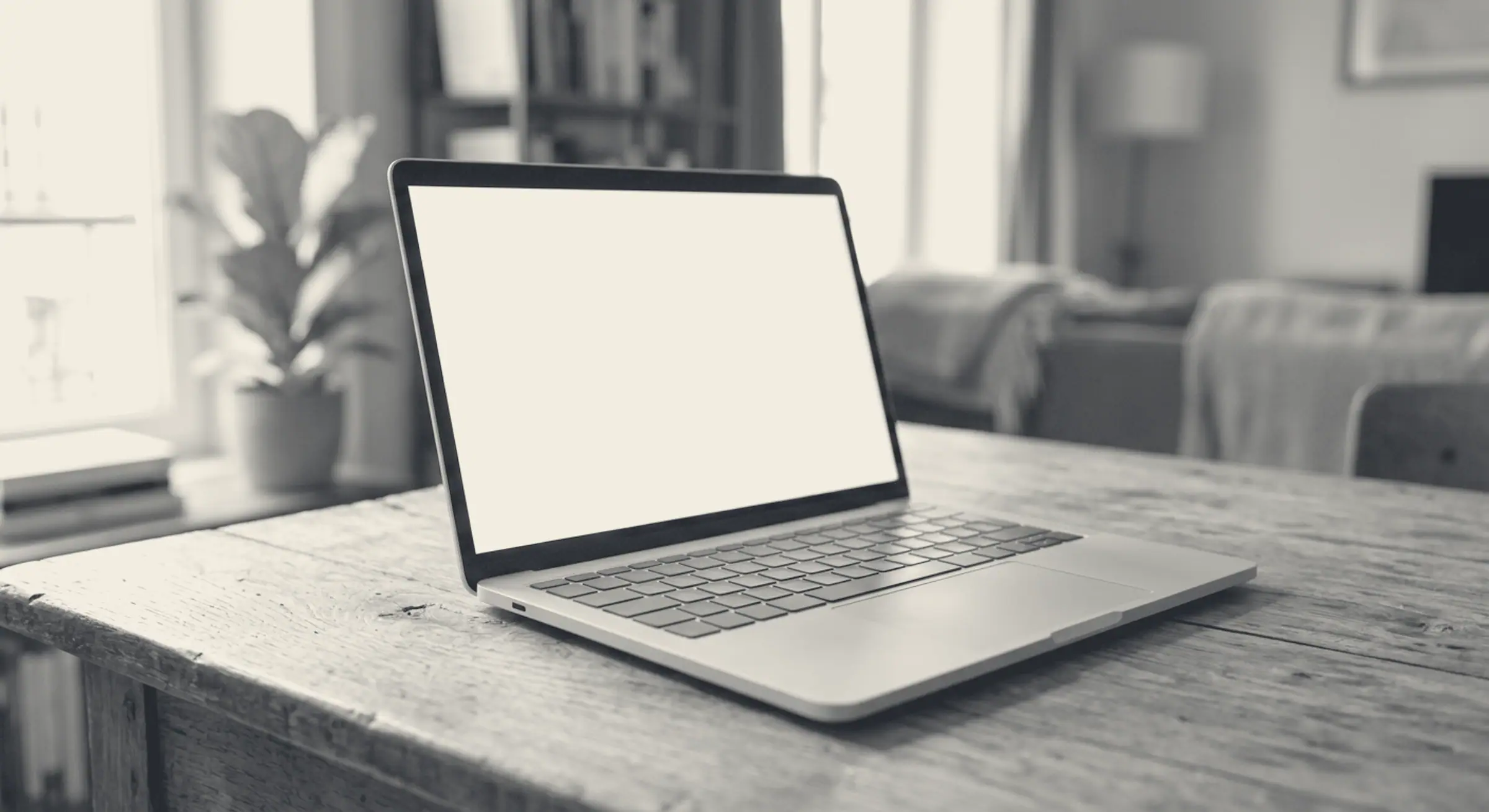 Erzeugtes Bild: ein aufgeklapptes Notebook mit leerem hellem Bildschirm auf einem Holztisch, der Raum dahinter in Unschärfe. Schwarzweiss in den Farben der Seite.