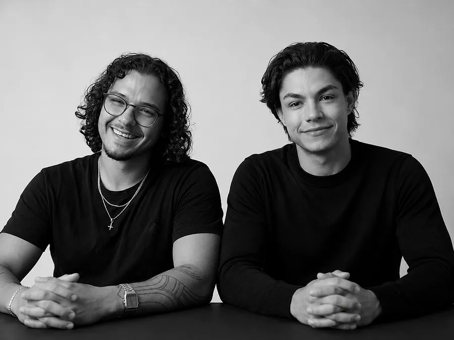 Dominik links und Moritz rechts, die beiden Gründer von Business Digital Solutions, nebeneinander an einem Tisch. Schwarzweisse Aufnahme.