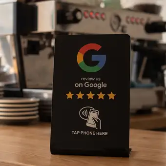 Erzeugte Ansicht: schwarzer NFC-Aufsteller auf der Theke eines Cafés, mit Google-Logo, fünf Sternen und der Aufschrift „Tap phone here“